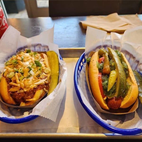 Two Hi Five Hotdogs, one chili cheese and one with pickles and peppers, on a metal tray.
